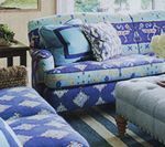 Blue patterned couch and ottoman in a living room, with striped rug and pillows.