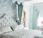 Bedroom with light blue floral wallpaper, a tufted headboard, and matching bedding.