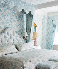 Bedroom with matching blue floral wallpaper, bedding, and curtains.