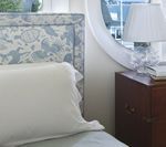 Bedroom detail with blue patterned headboard, white pillow, wooden nightstand, and lamp.
