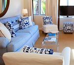 Living room with blue and white decor; sofa, chairs, patterned pillows, glass table.