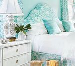 Bedroom with turquoise patterned headboard, curtains, pillows, and white bedding, with white nightstand.