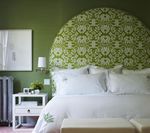 Bedroom with a large, patterned green headboard, white bedding, and green walls. A white nightstand sits to the side.