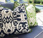 Three patterned pillows on a blue outdoor sofa near a pool.