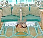 Teal outdoor sofa with four pillows, glass table, and basket of items.