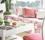 Bright living room with white sofa, red patterned fabric, and decorative pillows. White coffee table with decor.