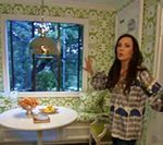 Woman in a green and white floral room, pointing. A small table sits next to a window.