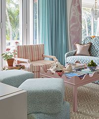 Coastal living room with blue, pink, and white accents, striped chair, patterned sofa, and surfboard decor.