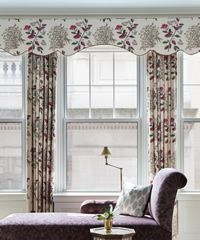 Elegant window with floral valance, patterned drapes, chaise lounge, and lamp.