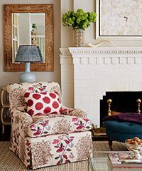 Floral armchair by a fireplace, with a red polka-dot pillow, a lamp, and a gold-framed mirror.