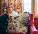 Floral pillows on a red sofa next to a window with floral curtains.