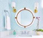 Bathroom with white sink, round mirror, blue patterned wallpaper, and gold sconces.
