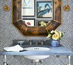 Bathroom vanity with blue countertop, patterned wallpaper, bamboo-framed mirror, and floral arrangement.