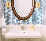 Bathroom with white sink, oval mirror, and blue patterned wallpaper.