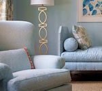 Light blue armchairs and a loveseat in a room with light blue walls, a gold lamp, and floral pillows.