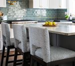 Three gray upholstered bar stools at a kitchen island, dark wood legs.