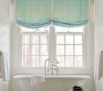 Bathroom window with light blue roman shades, over a white bathtub. White towels hang on both sides.