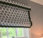 Roman shade with gray and white pattern and green trim over a window.