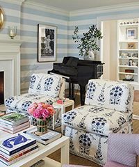 Living room with floral chairs, grand piano, and bookshelves. Blue and white color scheme.