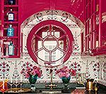 Bright pink bar with round window, floral tile backsplash, and bottles of alcohol on shelves.