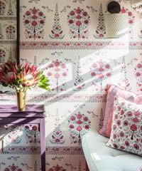 Room interior with floral wallpaper, a purple table, vase of flowers, and a pillow.