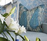 White lilies in vase, two blue patterned pillows on light blue couch.