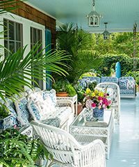 A porch with white wicker furniture, blue and white patterned cushions, and potted plants.