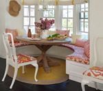 Round dining nook with built-in bench seating, round table, white chairs, and floral patterned cushions; bright, airy, and inviting.
