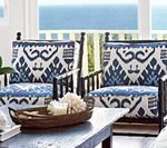 Two chairs with blue and white patterned cushions, a wooden tray with decor on a table, and a view of the sea.