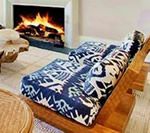 Cozy living room with a lit fireplace behind a wooden chair with patterned blue cushions.