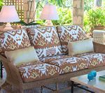 Wicker sofa with patterned cushions on a patio, with lamps, pillows, and a table.