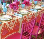 Brightly colored table setting with pink chairs, orange tablecloth, and blue glassware.