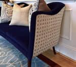 Navy velvet loveseat with tufted beige back, wooden legs, and decorative pillows on a patterned rug.
