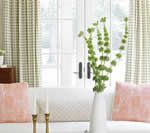 White sofa with pink pillows, green vase of flowers, and gold candlesticks. Window with light green checked curtains.