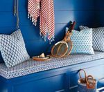 Blue built-in bench with patterned cushions, tennis rackets, and red striped towel against a blue wall.