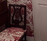 Dark wood chair with lyre back, red and white floral seat, against red toile wallpaper.