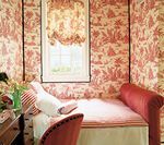 Bedroom with red toile wallpaper, daybed, and window with patterned shade.