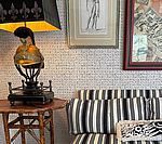 Lamp with bust on a small table next to a striped sofa, art on the wall.