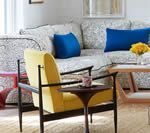 Yellow armchair with black frame and side table, in a living room with patterned sofa and blue pillows.