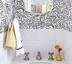 Bathroom with white subway tiles, patterned wallpaper, and yellow towels hanging.