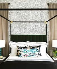 Canopy bed with green headboard, patterned wallpaper, and neutral drapes.