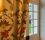 Curtain with floral pattern, covering part of a white door with a window looking out to greenery.