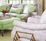 Living room with floral patterned sofa, green ottoman, and light purple chair.