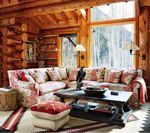 Cozy cabin living room with sectional sofa and large windows, surrounded by wooden beams and a snowy view.