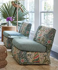 Two patterned armchairs in a bright room with a palm leaf and decorative table.