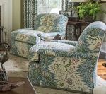 Two patterned armchairs in a living room, with a window and side table in the background.