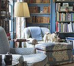 Cozy reading nook with a pug on an ottoman, surrounded by bookshelves and armchairs.