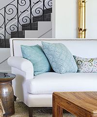 White sofa with blue pillows in front of a staircase and a decorative brass object.