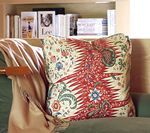 Pillow with a red and cream floral pattern on a green couch, with a tan blanket. Bookshelf in the background.
