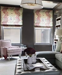 Living room with patterned window shades, upholstered furniture, and decorative ottoman.